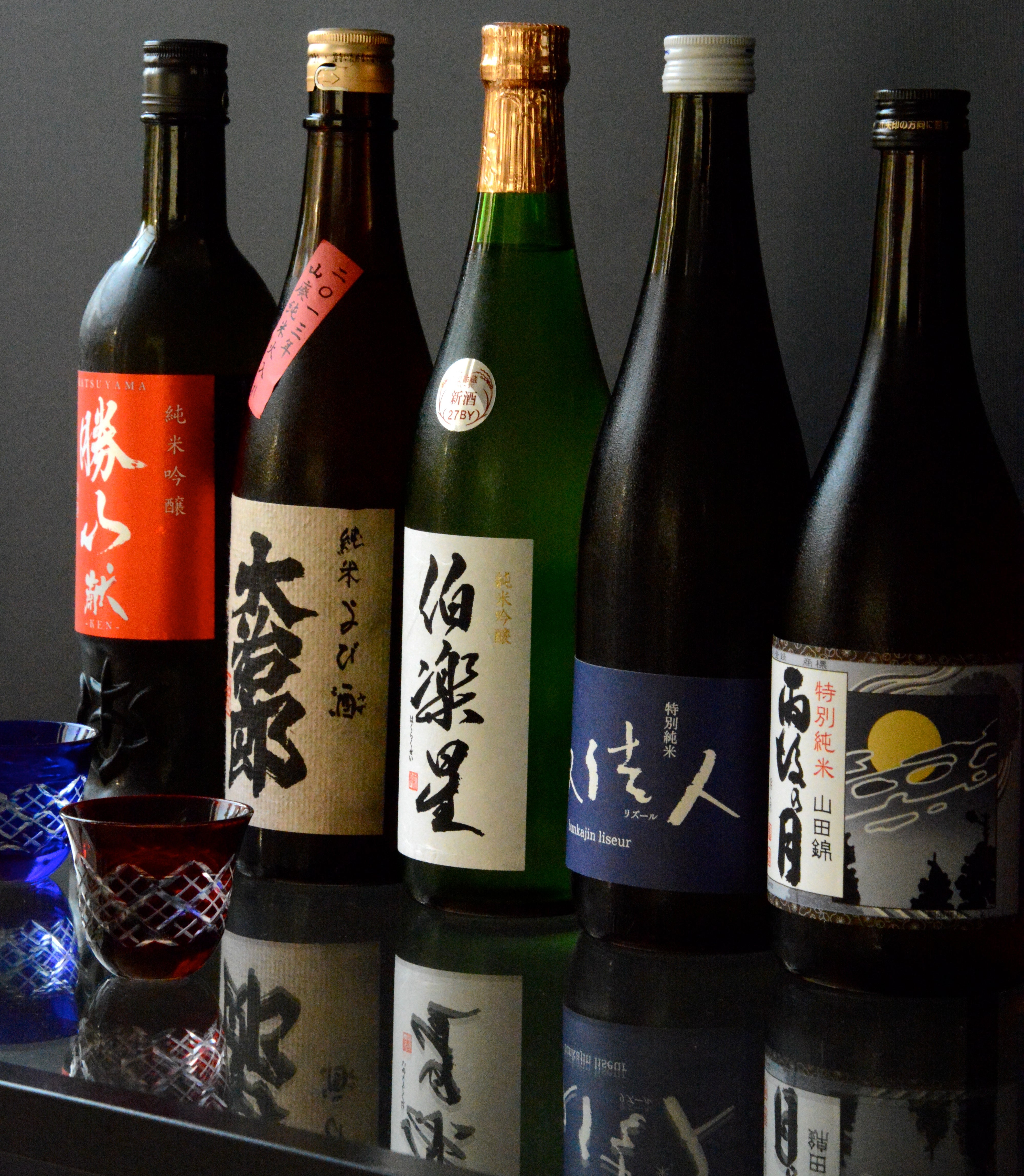 Collection of various bottles with labels on a reflective surface against a dark background